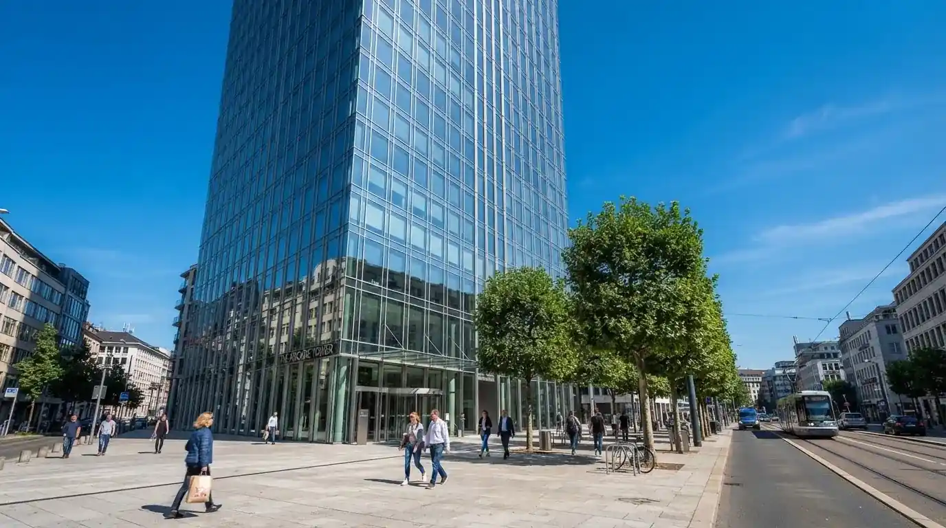 Edificio de oficinas moderno con fachada de cristal bajo un cielo despejado, gente caminando por la acera en una calle de ciudad.