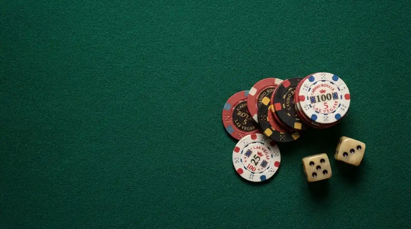 Vista cenital de fichas de casino y dados sobre una mesa de fieltro verde bajo luz suave.