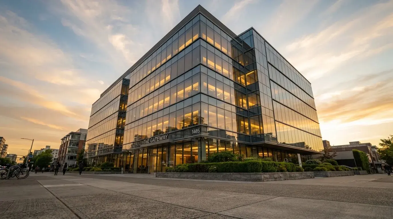 Un edificio de oficinas con fachada de cristal reflejando nubes, fotografiado desde una acera ancha por la tarde.
